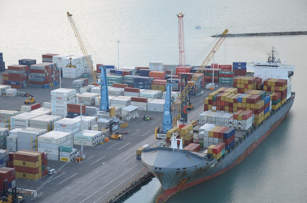 A Cargo Ship Being Loaded at a Dock Featuring Stacked Containers, Overhead Cranes, and Other Material Handling Equipment