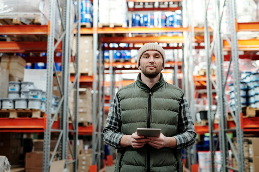 A man holding a tablet is standing in a warehouse